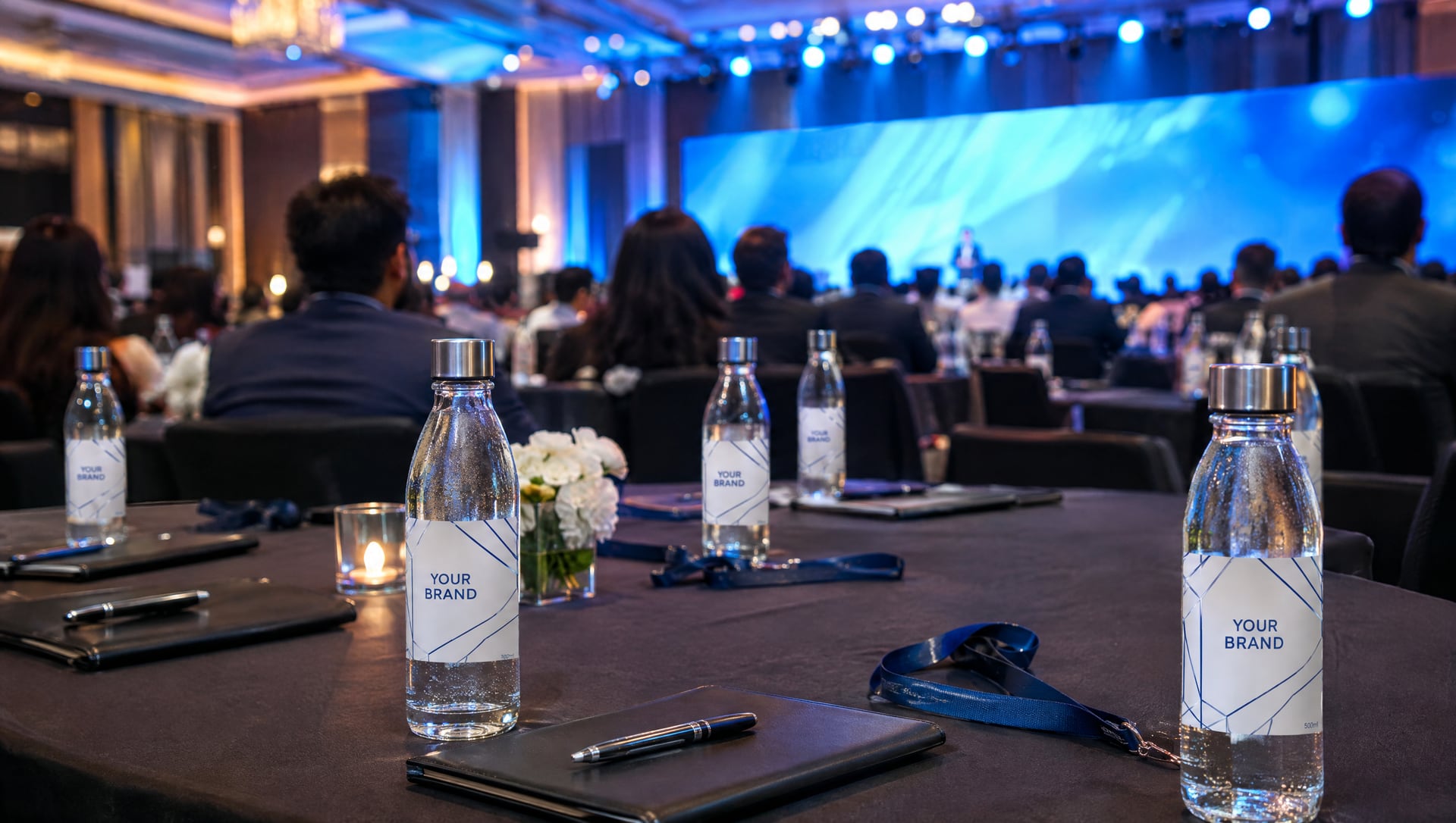 Glass bottles labelled YOUR BRAND on delegate tables at a corporate summit